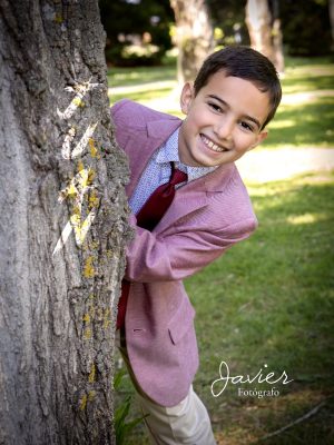 niño sonriente en sesión de Comunión en Valladolid apoyado en un árbol en exterior